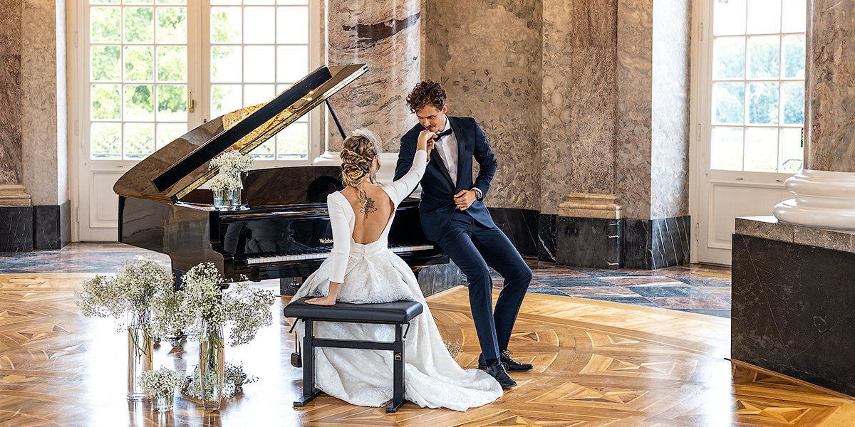 bilderschlag Braut sitzt am Klavier und Bräutigam küsst sie